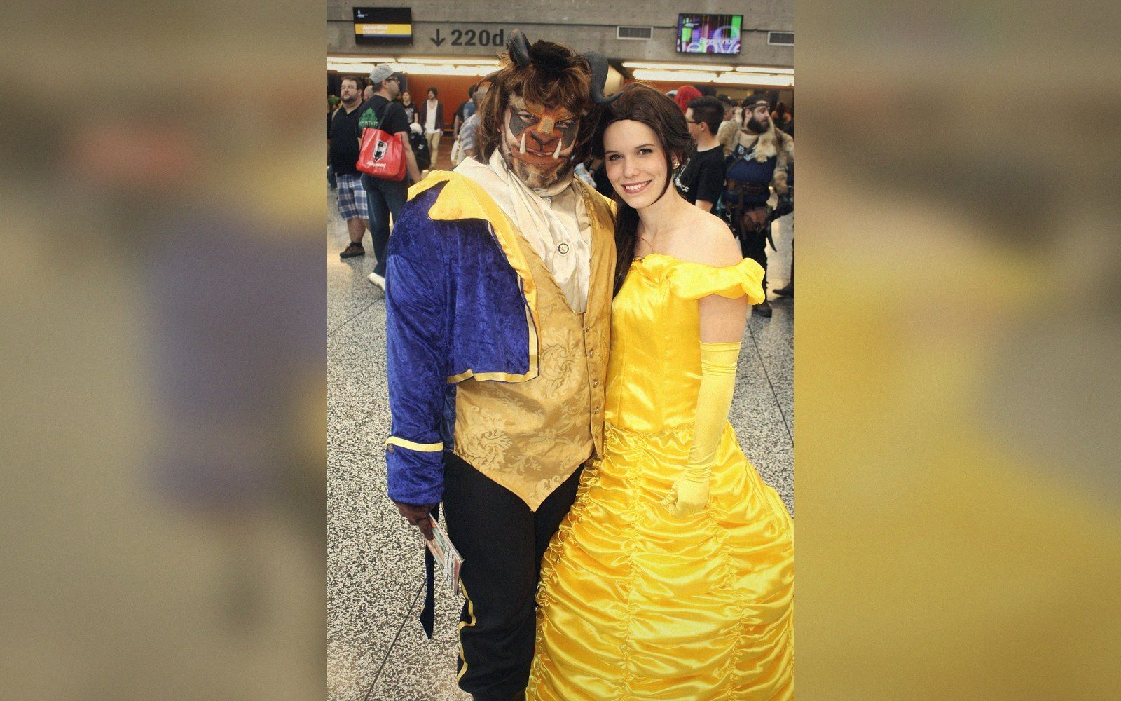 Cosplayers dressed as Belle and the Beast pose together at a convention hallway