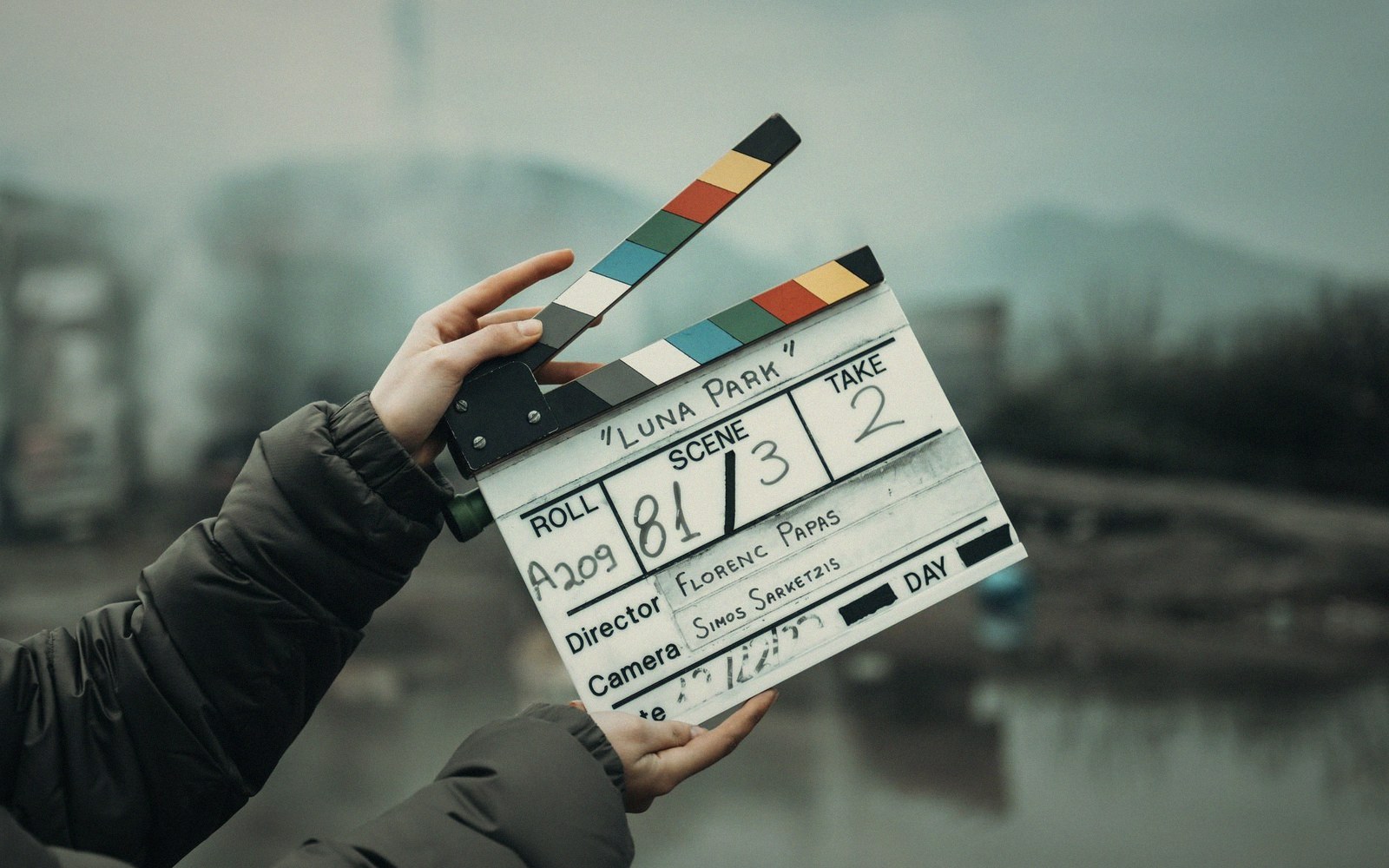 Hands hold an open film clapperboard labeled "Luna Park" outdoors on a hazy day