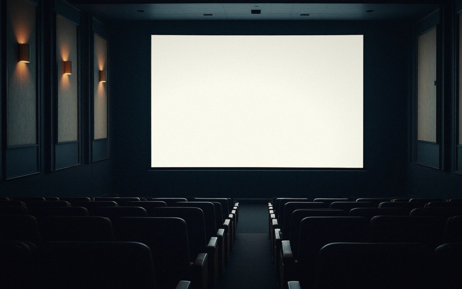 Empty theater seats face a blank white screen lit by dim wall sconces