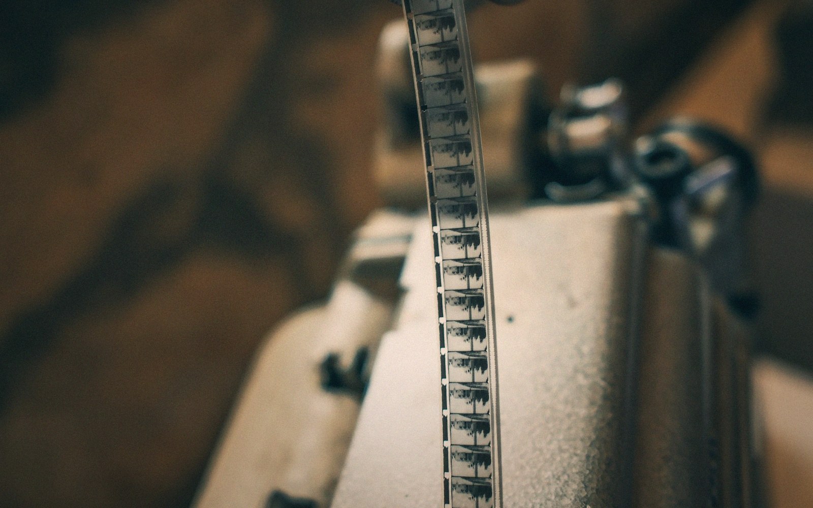 A strip of film with tiny frames threads through a vintage projector